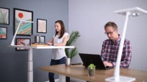 woman using a standing desk next to man sitting on a desk