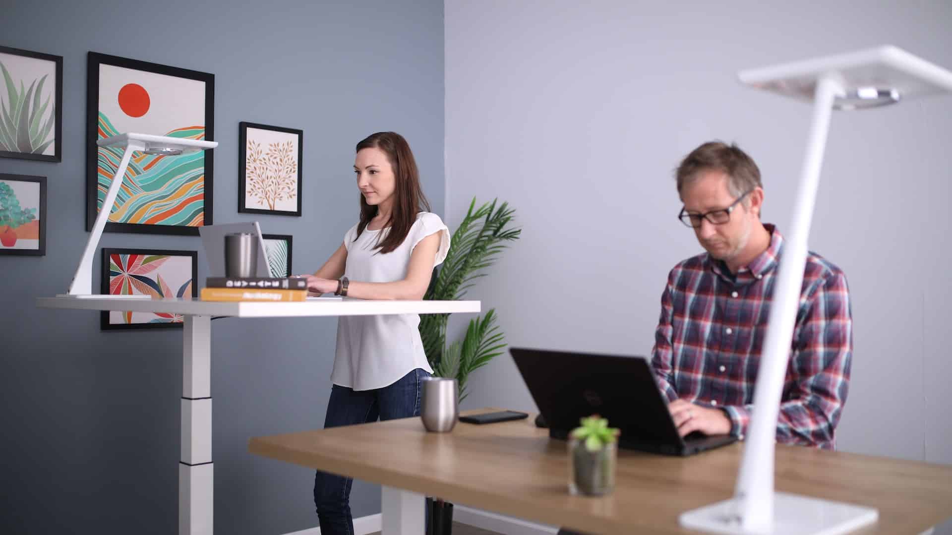 woman using a standing desk next to man sitting on a desk